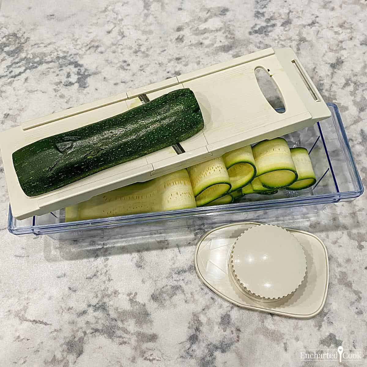 A zucchini squash being sliced into ribbons using a mandoline slicer.
