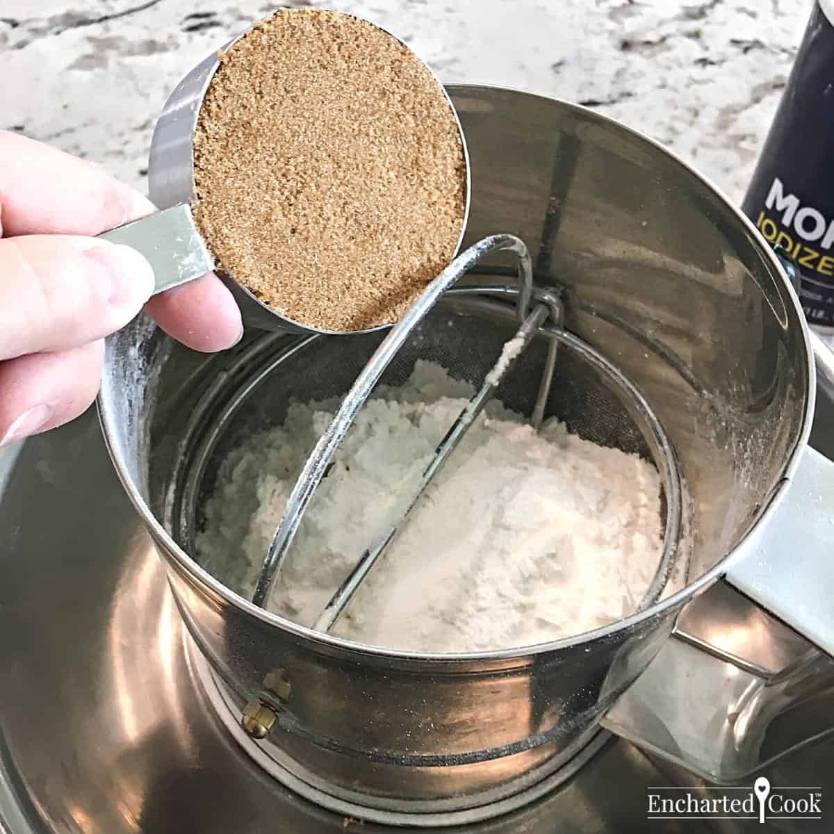 Brown sugar is fully packed into a measuring cup and added to the dry ingredients in a large sifter.