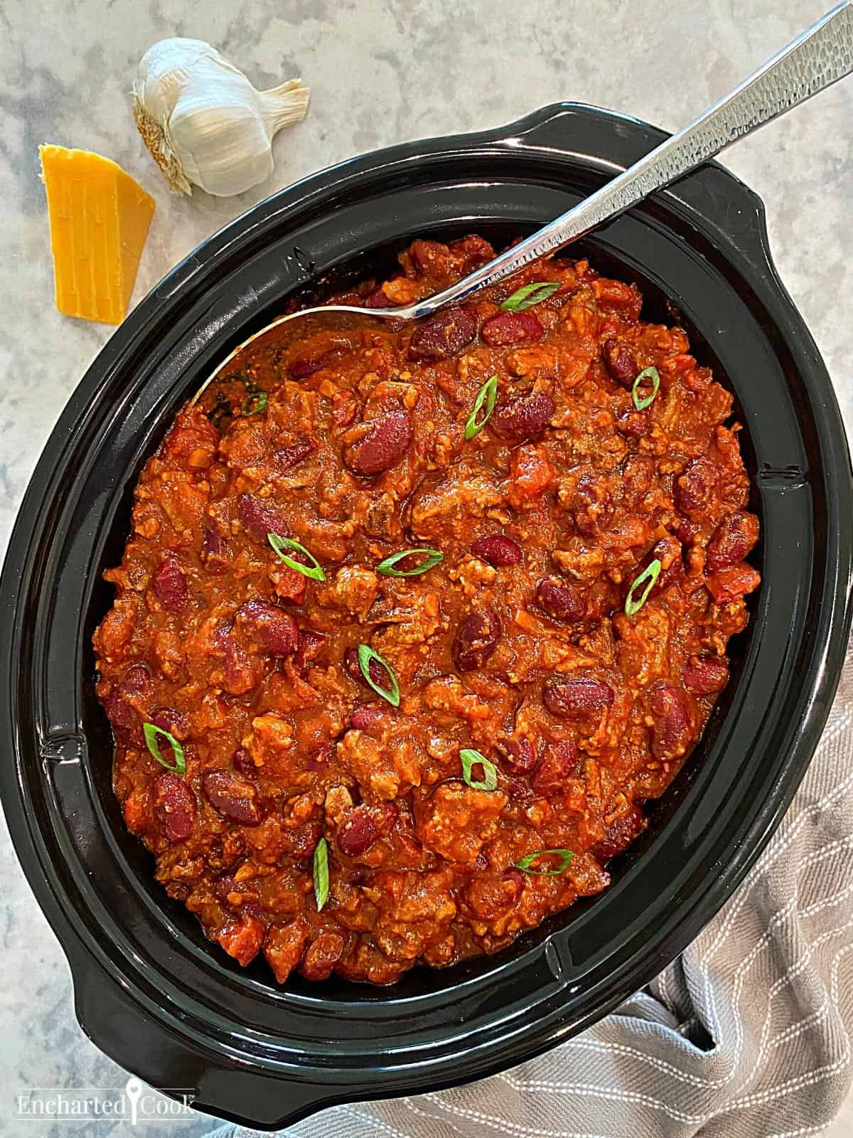 A black slow cooker filled with chili.