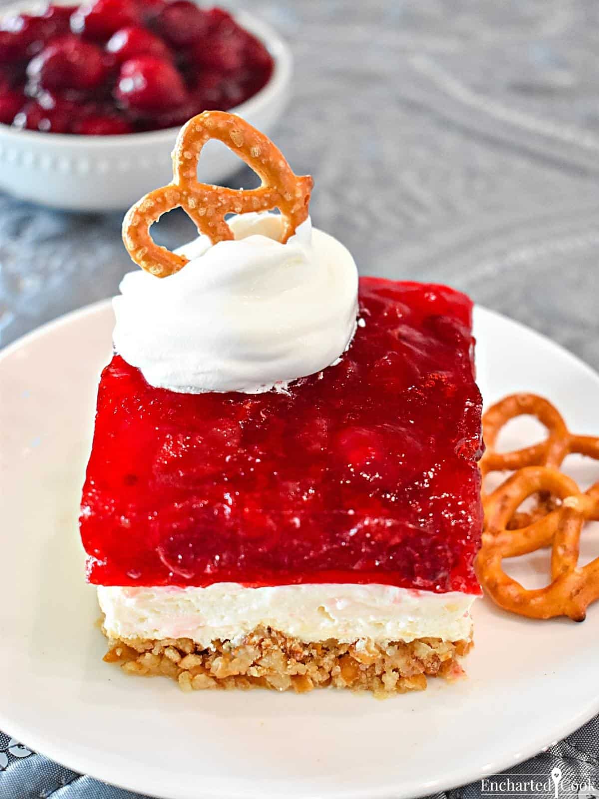 The cheesecake dessert on a plate and garnished with whipped topping and a small pretzel.
