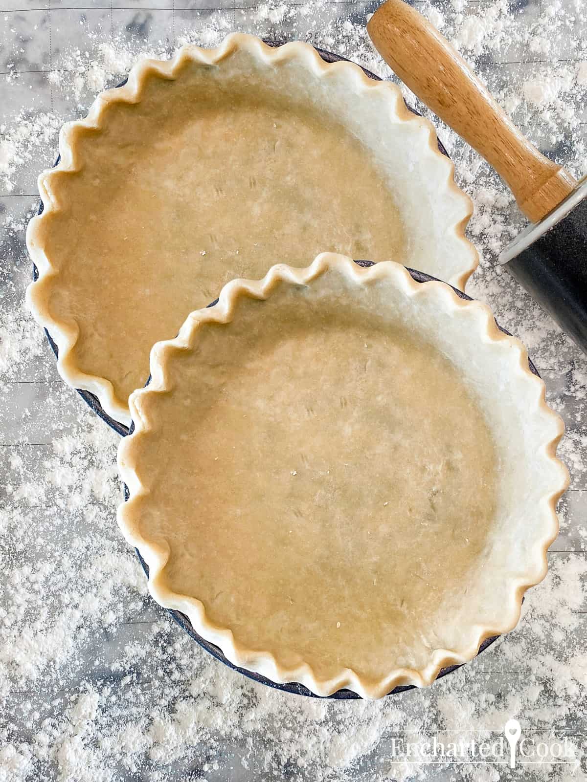 Two pie crust shells in pans on a floured surface with a rolling pin.