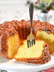 A bundt cake on a serving stand with a piece cut and on its side with a fork in it.