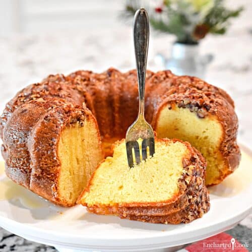 A bundt cake on a serving stand with a piece cut and on its side with a fork in it.