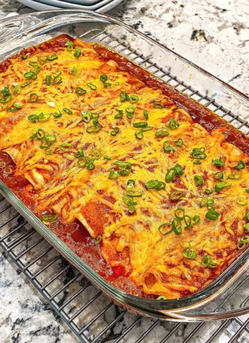 Square image of baked enchiladas covered in red sauce and smothered with cheese in a glass baking dish.