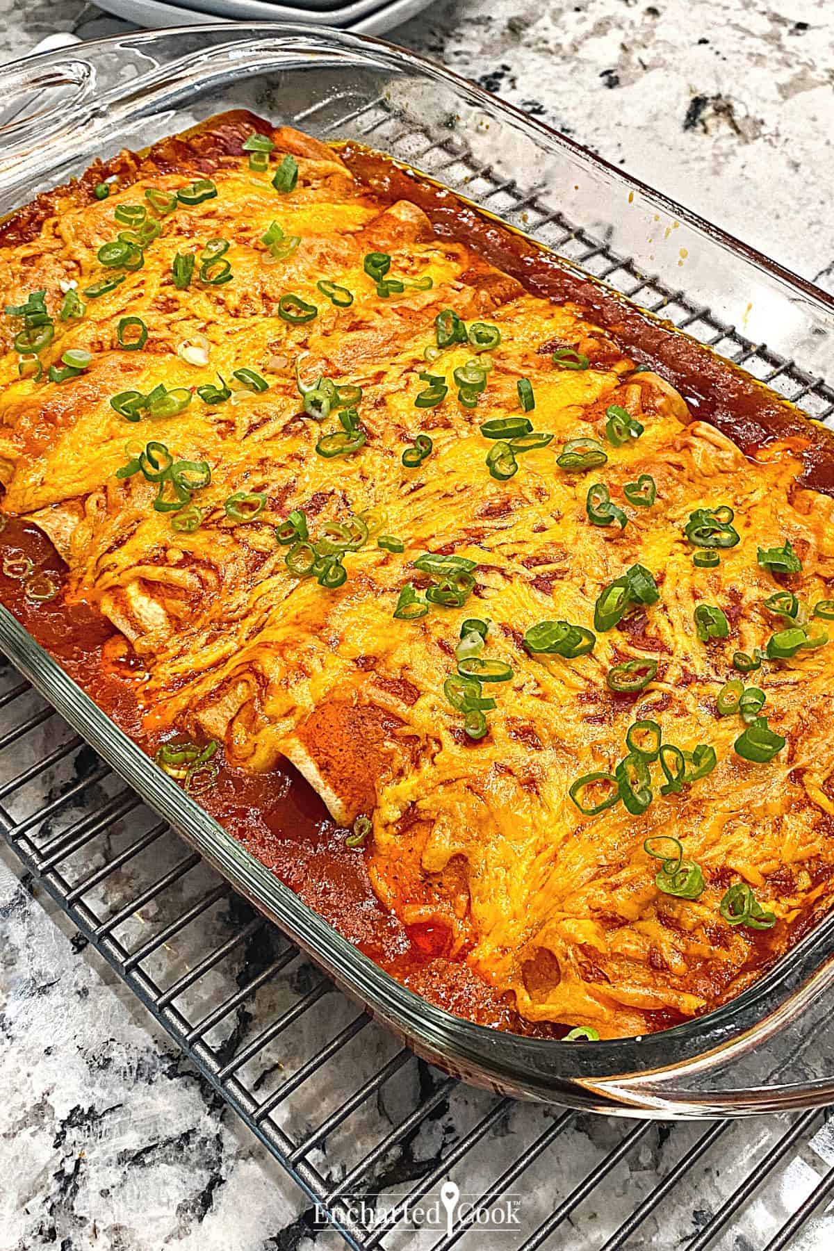 Baked enchiladas covered in red sauce and smothered with cheese in a glass baking dish.