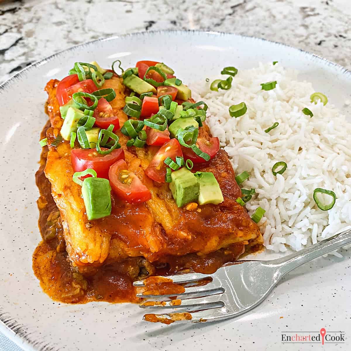 Enchiladas on a plate garnished with diced fresh tomatoes and avocado with a side of white rice.