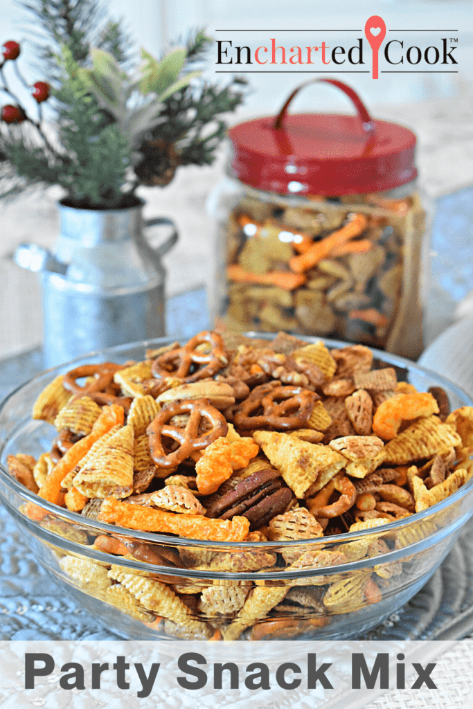 A clear glass bowl of party snack mix made with cereal, pretzels, nuts, cheese crisps, and bugle corn snacks with text overlay.