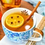 A hot toddy garnished with a slice of lemon studded with whole cloves and a cinnamon stick.