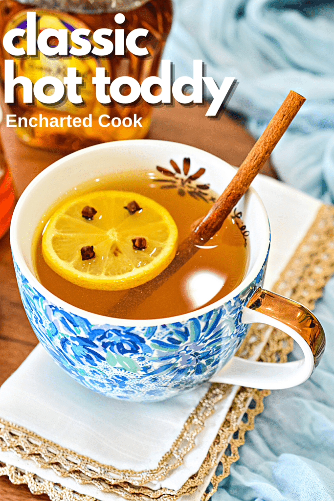 A hot toddy garnished with a slice of lemon studded with whole cloves and a cinnamon stick with text overlay.