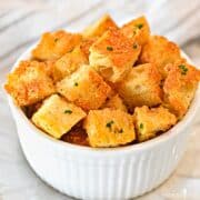Square image of garlic parmesan coated croutons in a white dish.