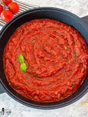 Overhead view of the cooked hearty marinara sauce in a Dutch oven garnished with fresh basil.