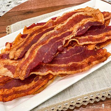 Cooked bacon on a white plate with a beige linen napkin.