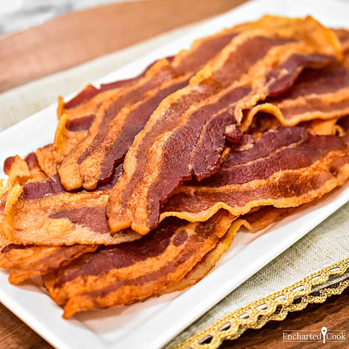 Close up view of cooked bacon on a white plate with a beige linen napkin.