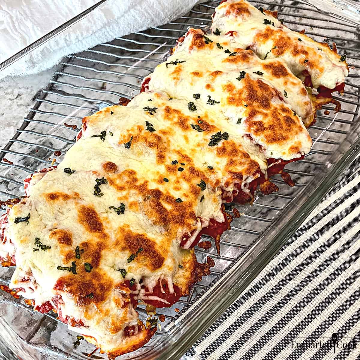 Chicken Tenders Parmesan are smothered in marinara sauce and topped with cheese in a glass baking dish.