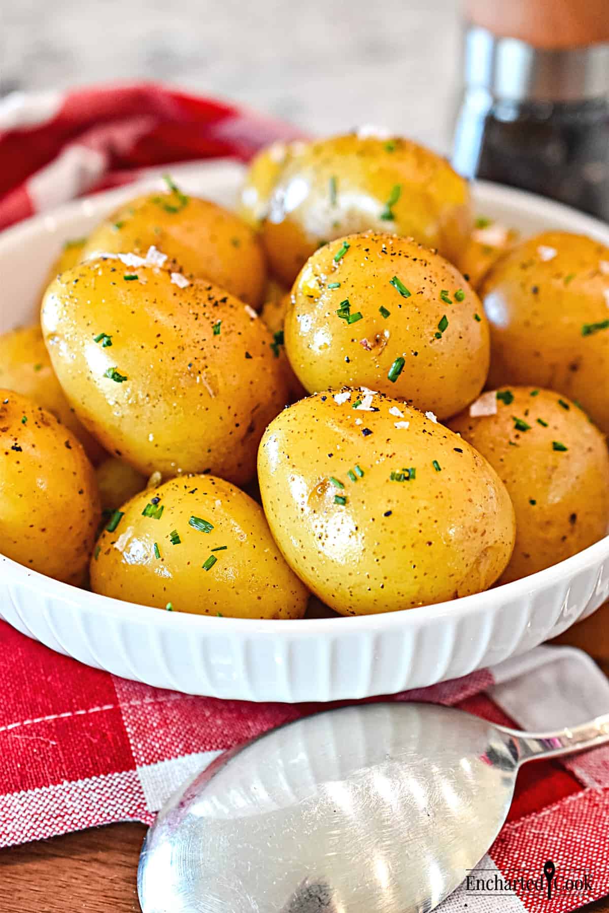 Boiled small whole golden potatoes in a white dish with a pepper mill and serving spoon.