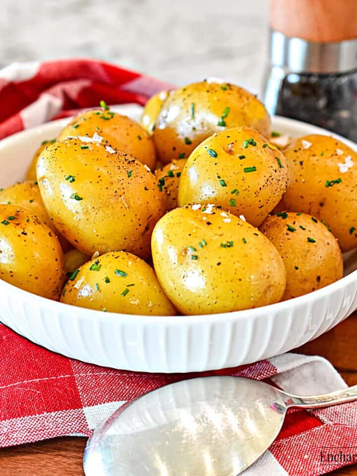 Boiled small whole golden potatoes in a white dish with a pepper mill and serving spoon.