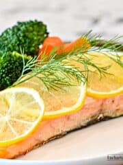 A fillet of Atlantic salmon with its skin on, cooked in butter and lemon on a white plate.