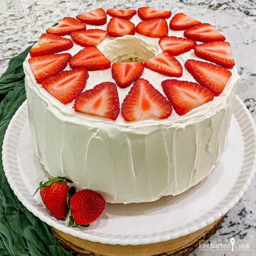 A tube cake in white frosting decorated with sliced strawberries on its top.