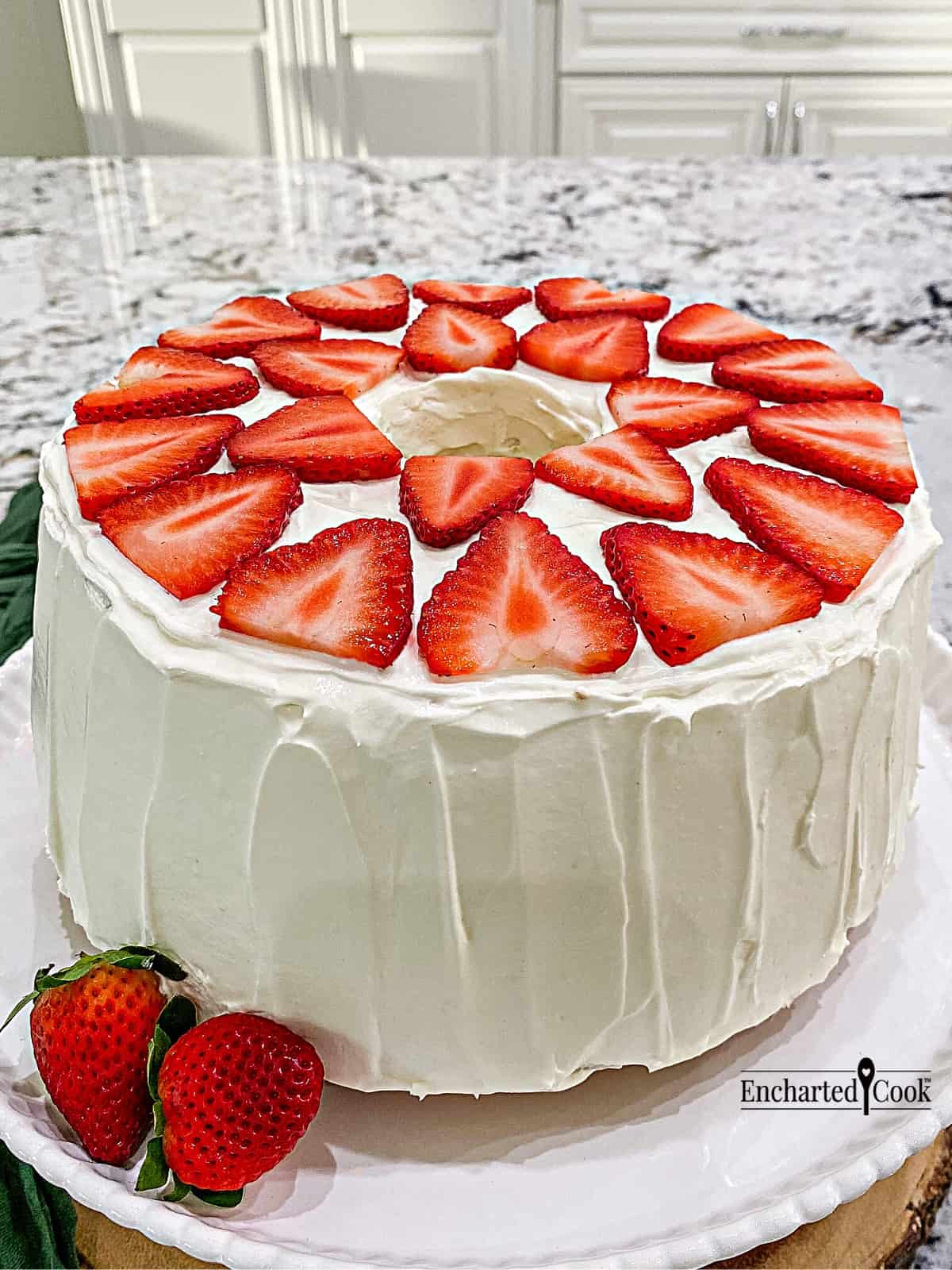 A tube cake in white frosting decorated with sliced strawberries on its top.