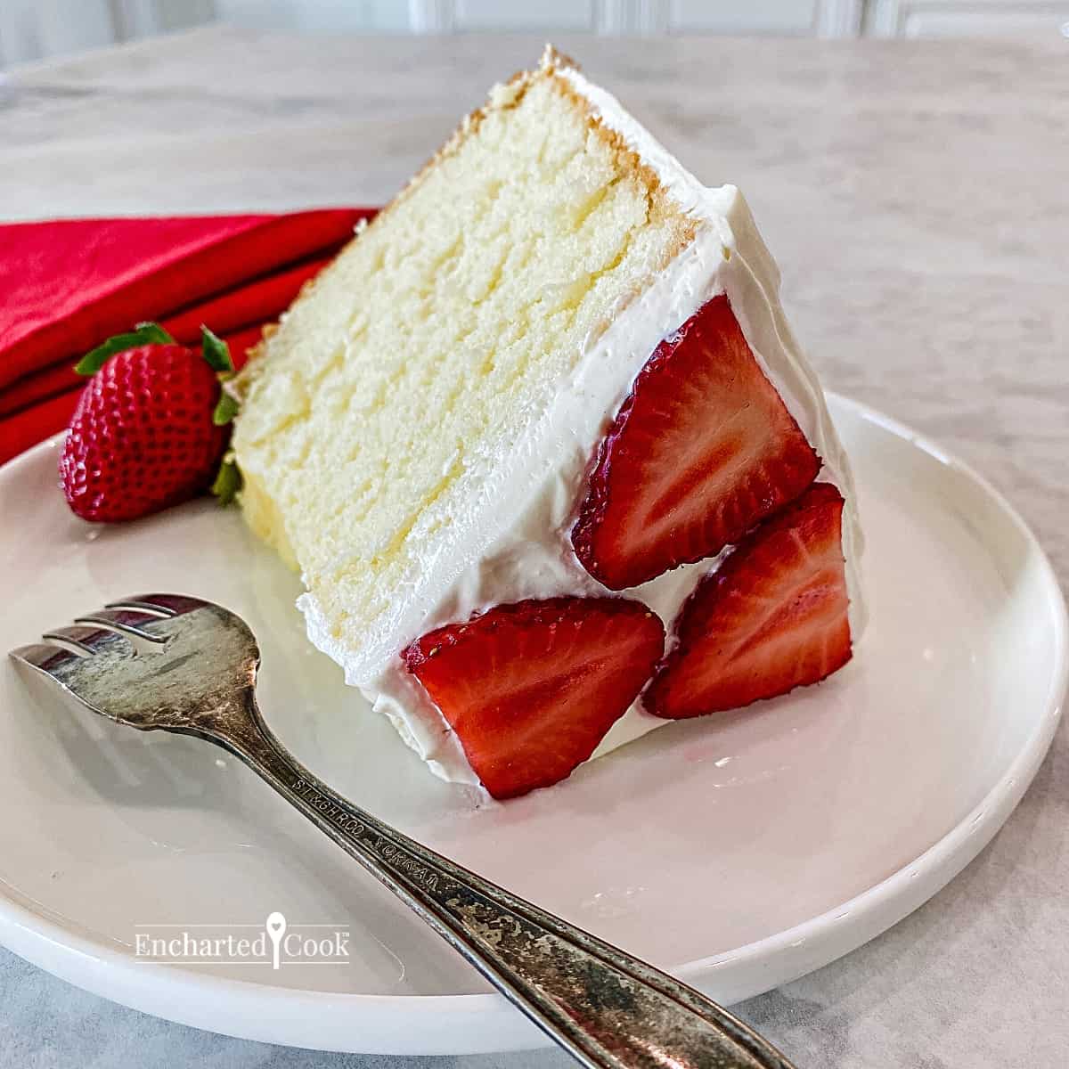 A slice of pale yellow cake with white frosting and decorated with sliced strawberries.