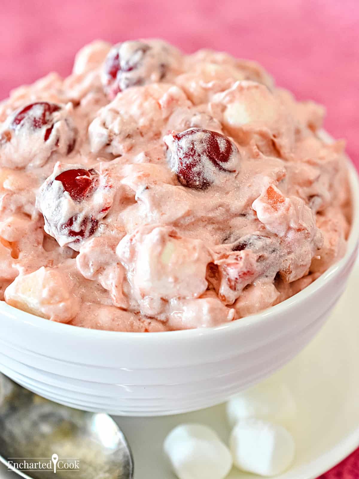 A white bowl contains pink fluff with marshmallows and cherries.