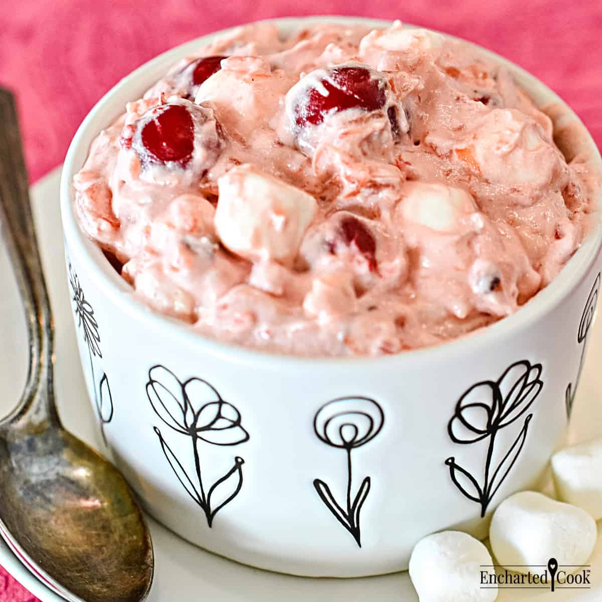 A white dish with black flowers contains a pink fluff with marshmallows and cherries.