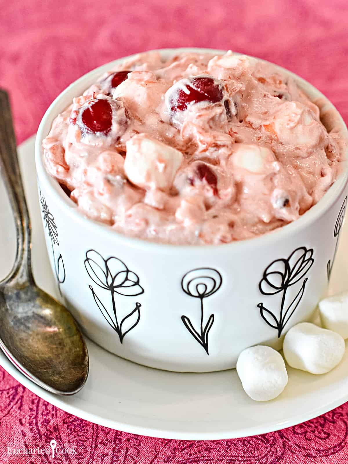 A white dish with black flowers contains a pink fluff with marshmallows and cherries.