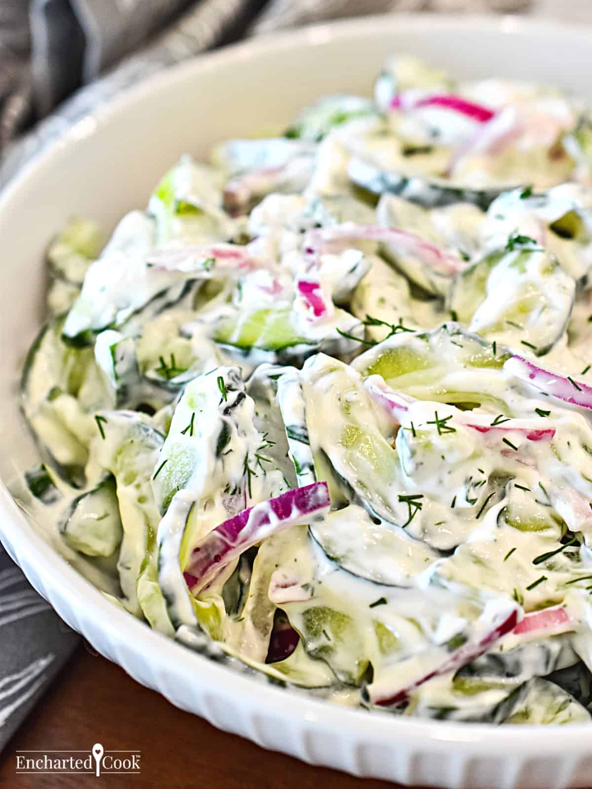 Sliced cucumber and red onion in a creamy dressing in a white bowl.