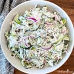 Sliced cucumber and red onion in a creamy dressing in a white bowl.