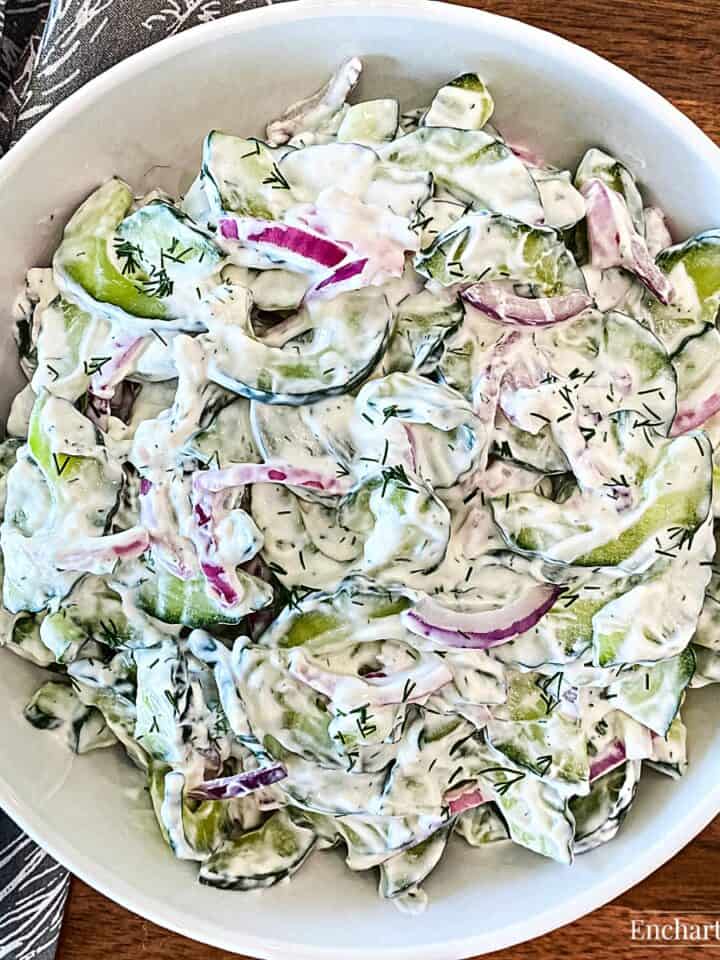 Sliced cucumber and red onion in a creamy dressing in a white bowl.