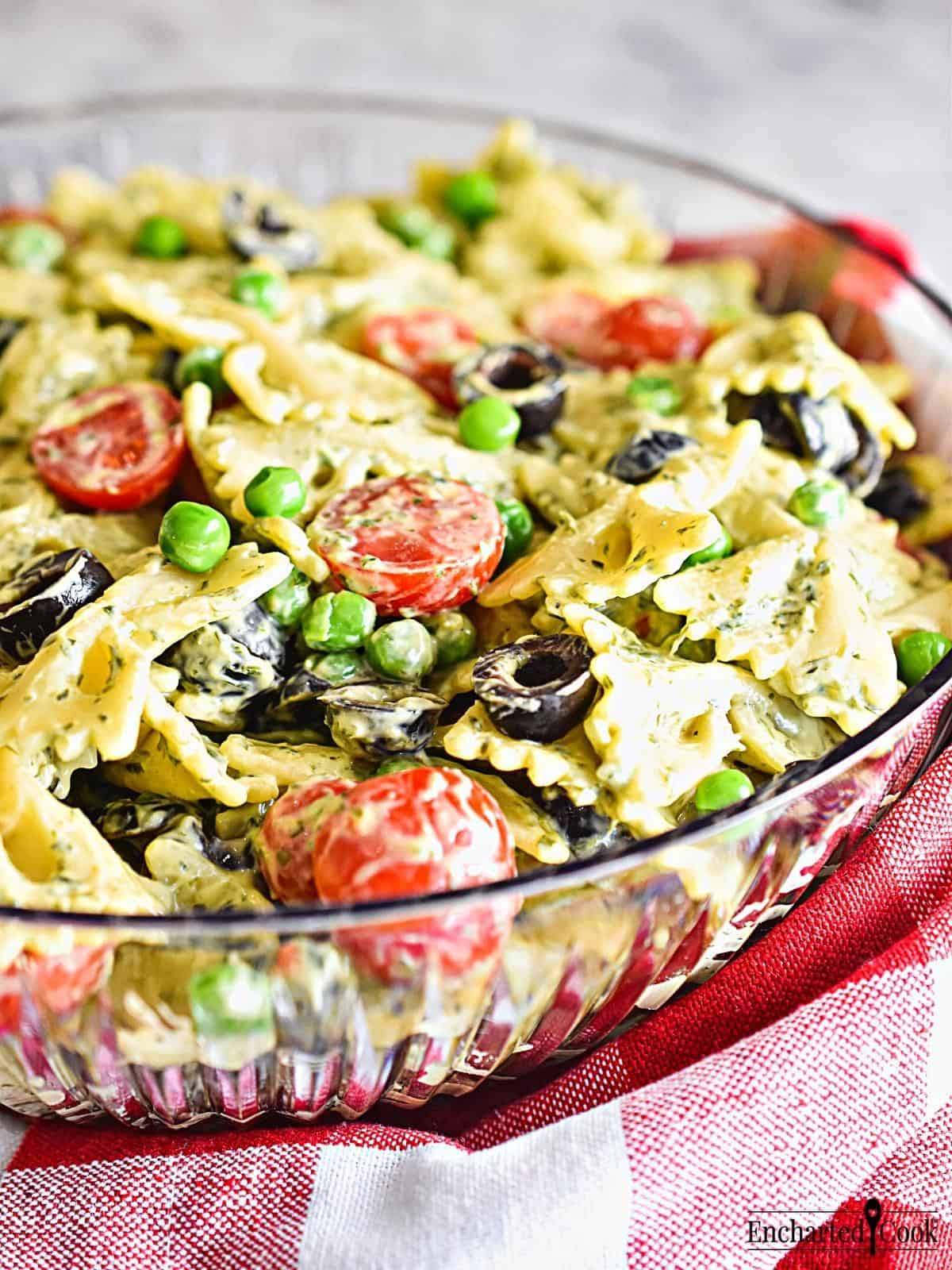 A clear bowl of Green Goddess Pasta Salad made with bow tie pasta with a red and white checked napkin.