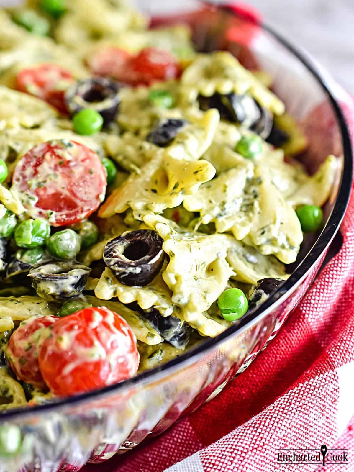 A close-up view of Green Goddess Pasta Salad made with bow tie pasta in a clear bowl with a red and white checked napkin.