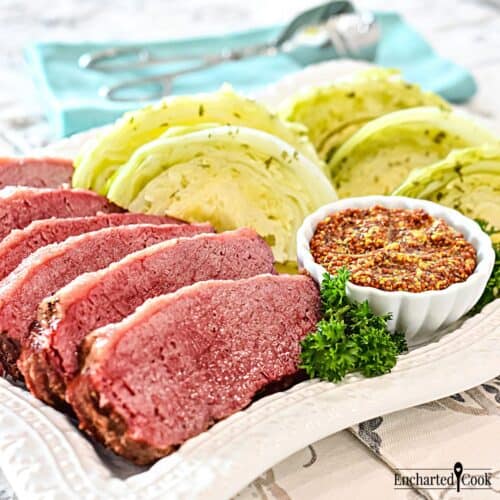Pink corned beef and green cabbage on a white platter with a dish of whole grain mustard.