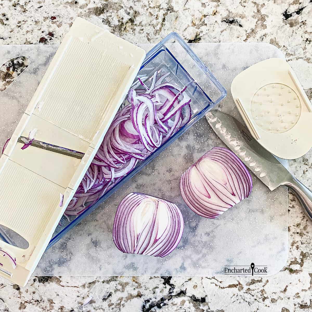 A red onion is cut with a knife and sliced thinly on a mandoline slicer.