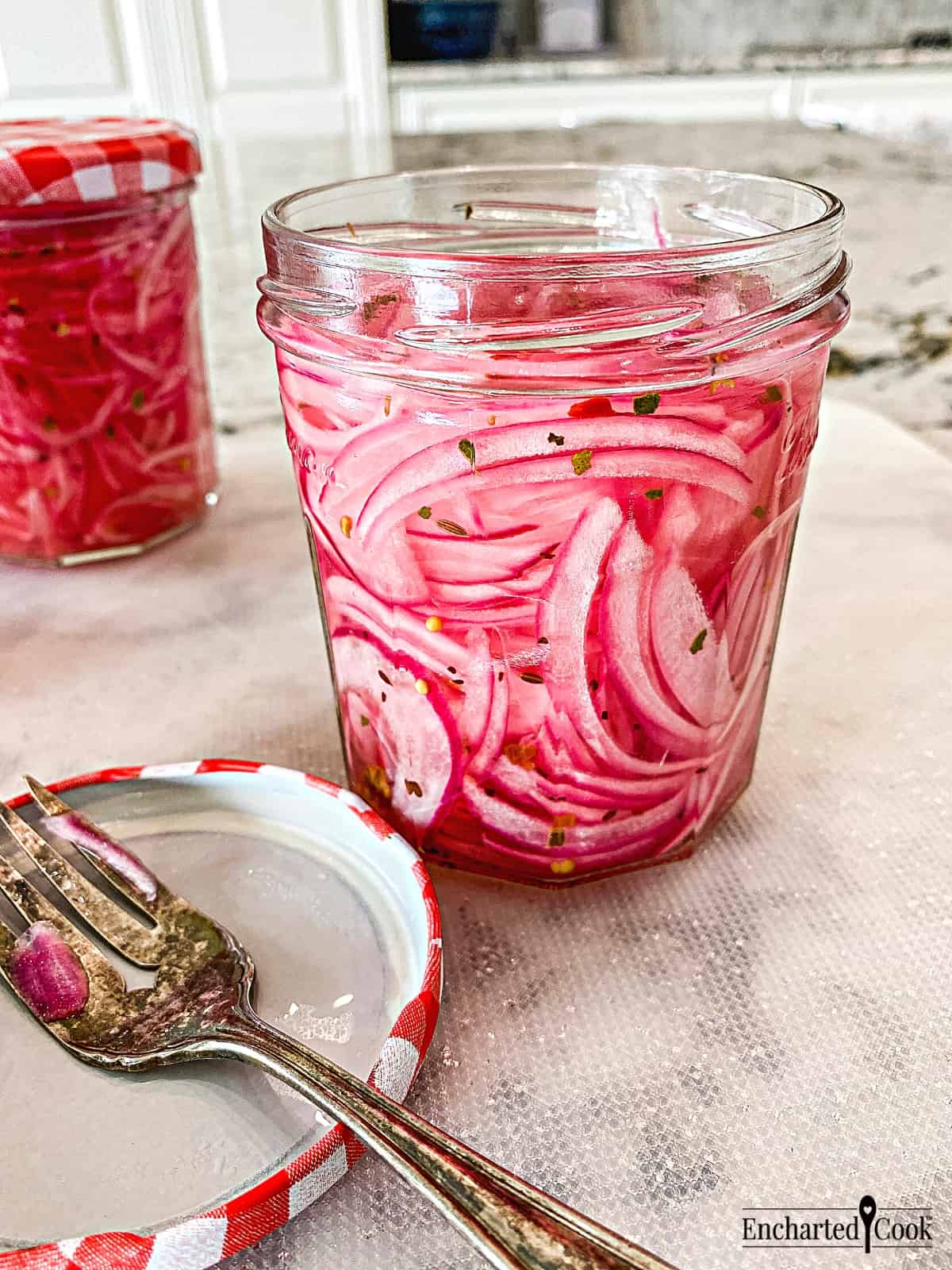 Slices of pink-colored pickled red onion in a jar with a jar lid and fork beside it.