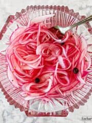 Slices of pink-colored pickled red onion in a fancy-cut glass dish with a fork.