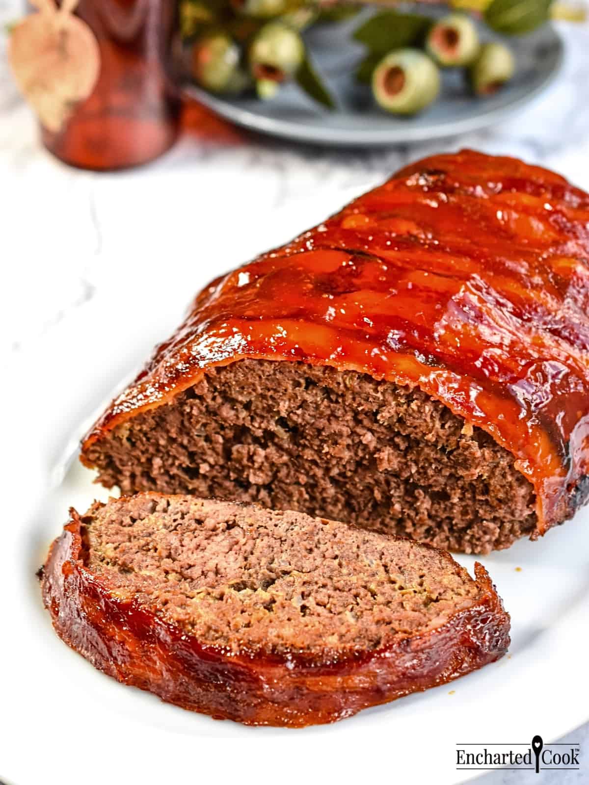 A bacon wrapped meatloaf is on a white platter.