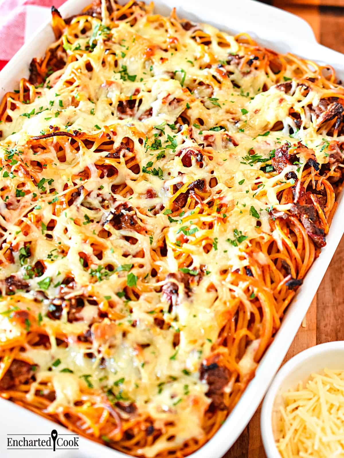 Spaghetti with marinara sauce topped with cheese in a white baking dish.