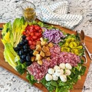 A board covered with romaine lettuce and other Italian salad ingredients.