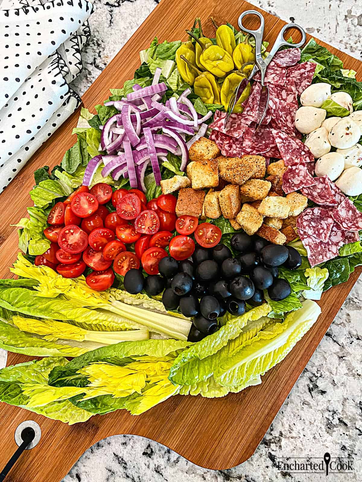 A large board covered with romaine lettuce and other Italian salad ingredients.