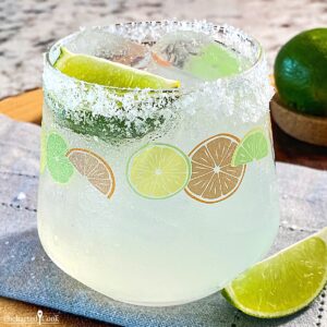 A margarita cocktail over ice in a glass with a salted rim garnished with a wedge of lime.