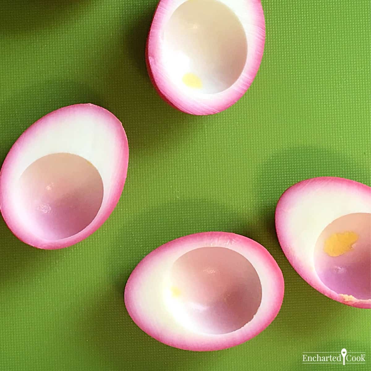 Pink-colored hard-cooked eggs are cut in half and the yolk is removed.