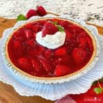 A whole strawberry pie topped with whipped cream on a white plate.