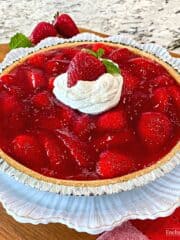 A whole strawberry pie topped with whipped cream on a white plate.