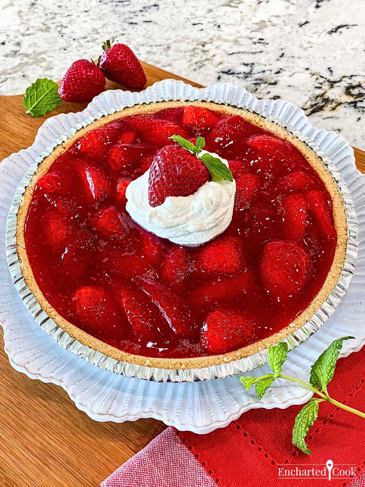 A whole strawberry pie topped with whipped cream on a white plate.