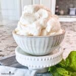 A grey bowl filled with perfectly whipped cream with stiff peaks.