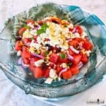 Watermelon Salad topped with feta cheese and lemon zest in a large green glass bowl.
