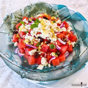 Watermelon Salad topped with feta cheese and lemon zest in a large green glass bowl.