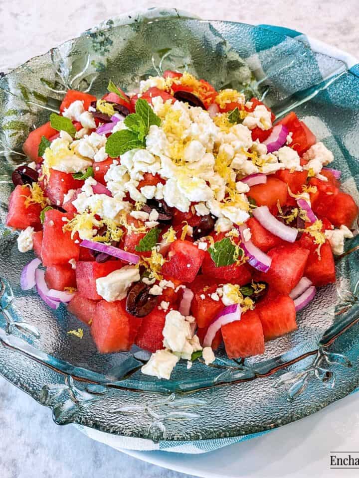 Watermelon Salad topped with feta cheese and lemon zest in a large green glass bowl.