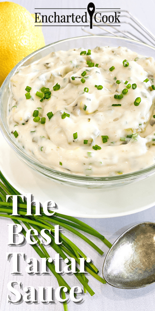 Tartar sauce in a clear glass bowl on a white plate encircled by a lemon, fresh whole chives, a small whisk, and a spoon with text overlay.